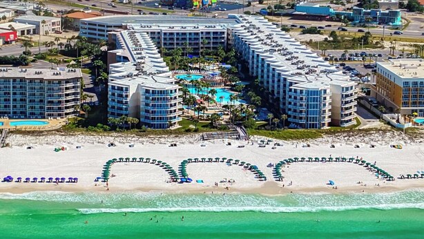 A resort with multiple hotel buildings, a central pool area, and a beach with umbrellas.