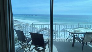 A balcony with a view of the beach and pier, furnished with chairs and a table.