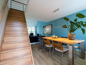 Ein modernes Interieur mit einer Holztreppe, einer Essecke mit Tisch und Stühlen sowie einer großen Kübelpflanze.