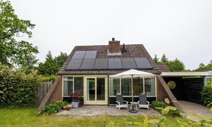 A house with solar panels, a glass door entrance, a patio with chairs, and a number '117' sign.