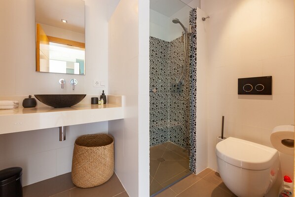 A modern bathroom with a white sink, a vessel basin, a large mirror, a toilet, and a shower with a patterned glass door.