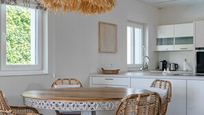 A modern kitchen with white cabinetry, a round wooden table, wicker chairs, and a hanging light fixture. - Villa in Marbella Near Beach (Marbella)