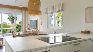 A modern kitchen with a large island, wicker hanging light, and a view of the outdoors. - Villa in Marbella Near Beach (Marbella)