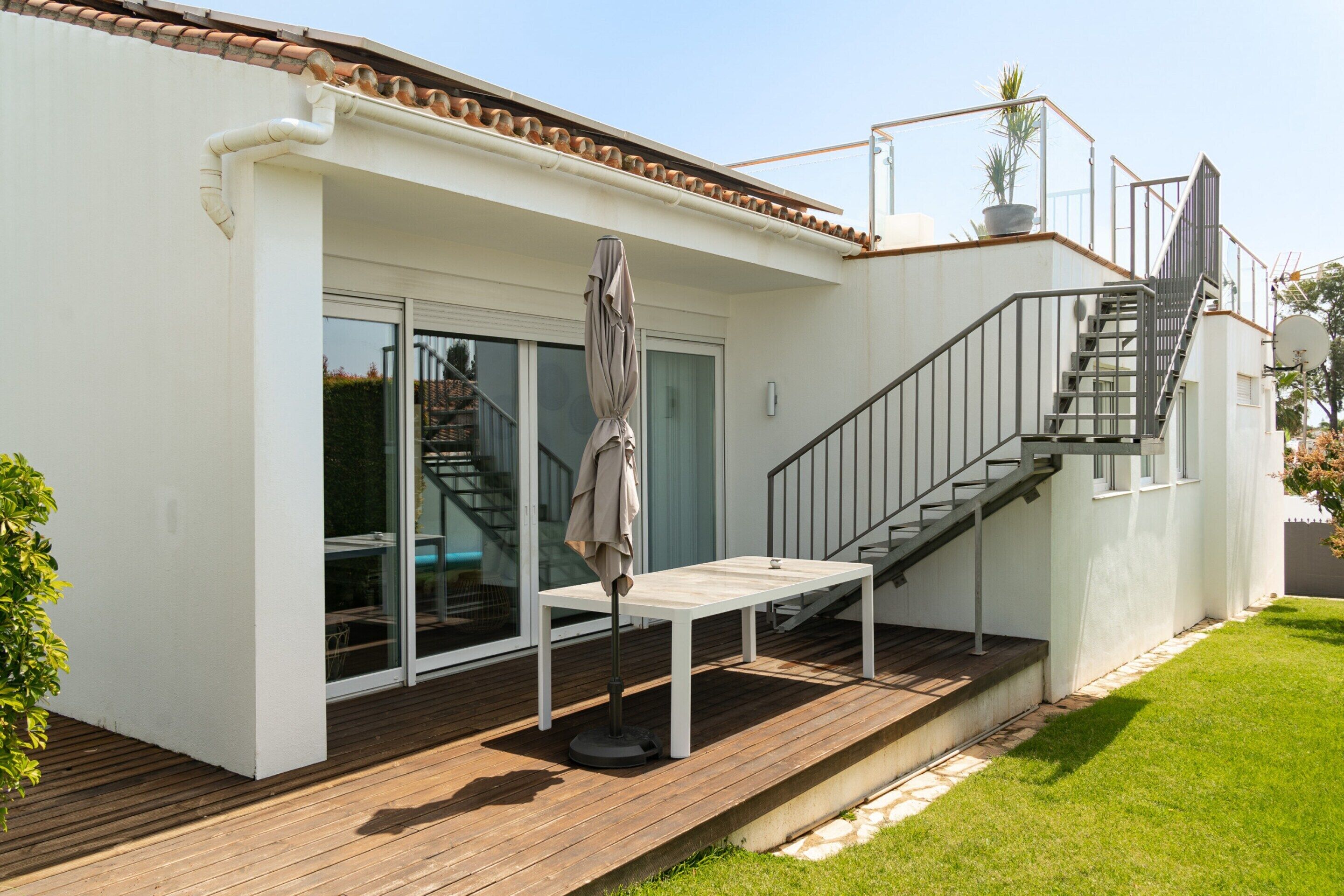 Una casa moderna con terraza de madera, escaleras y puerta corrediza de vidrio.