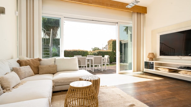 A modern living room with a large sofa, a TV, and a dining area visible through glass doors. - Villa in Marbella Near Beach (Marbella)