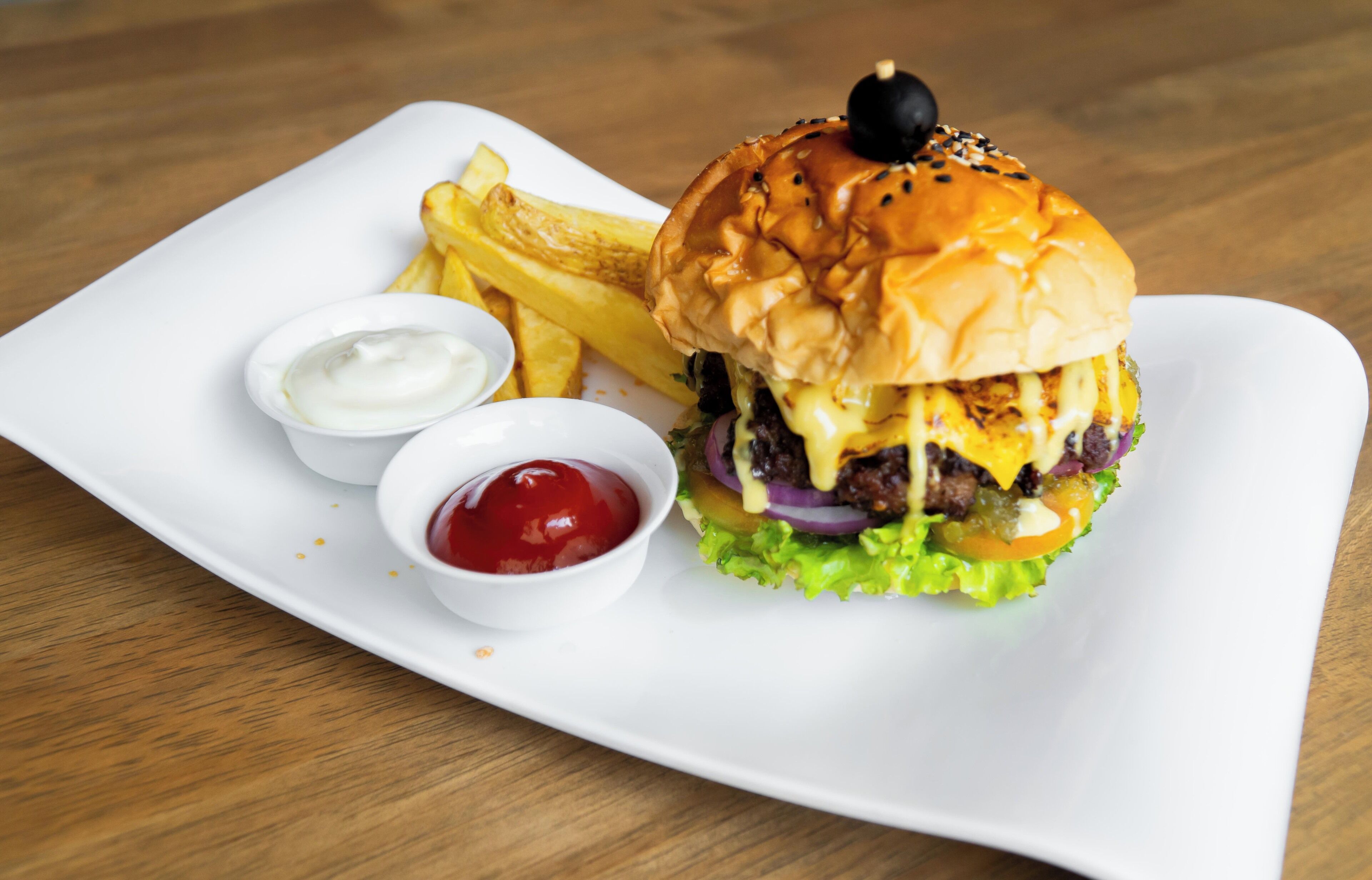 A burger with fries and two dipping sauces on a white plate.