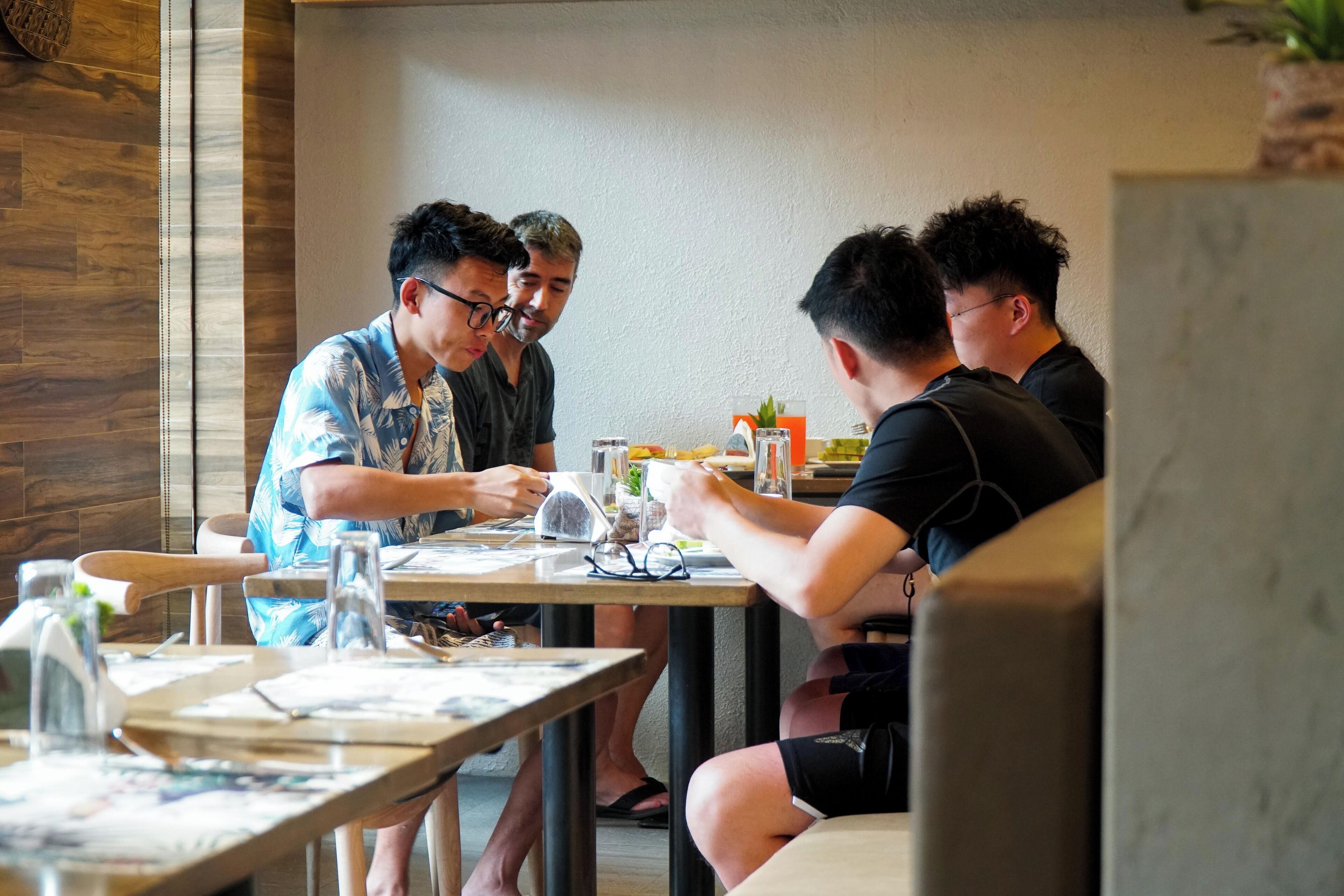 A group of people dining at a table in a restaurant with wooden flooring and a simple, modern decor.