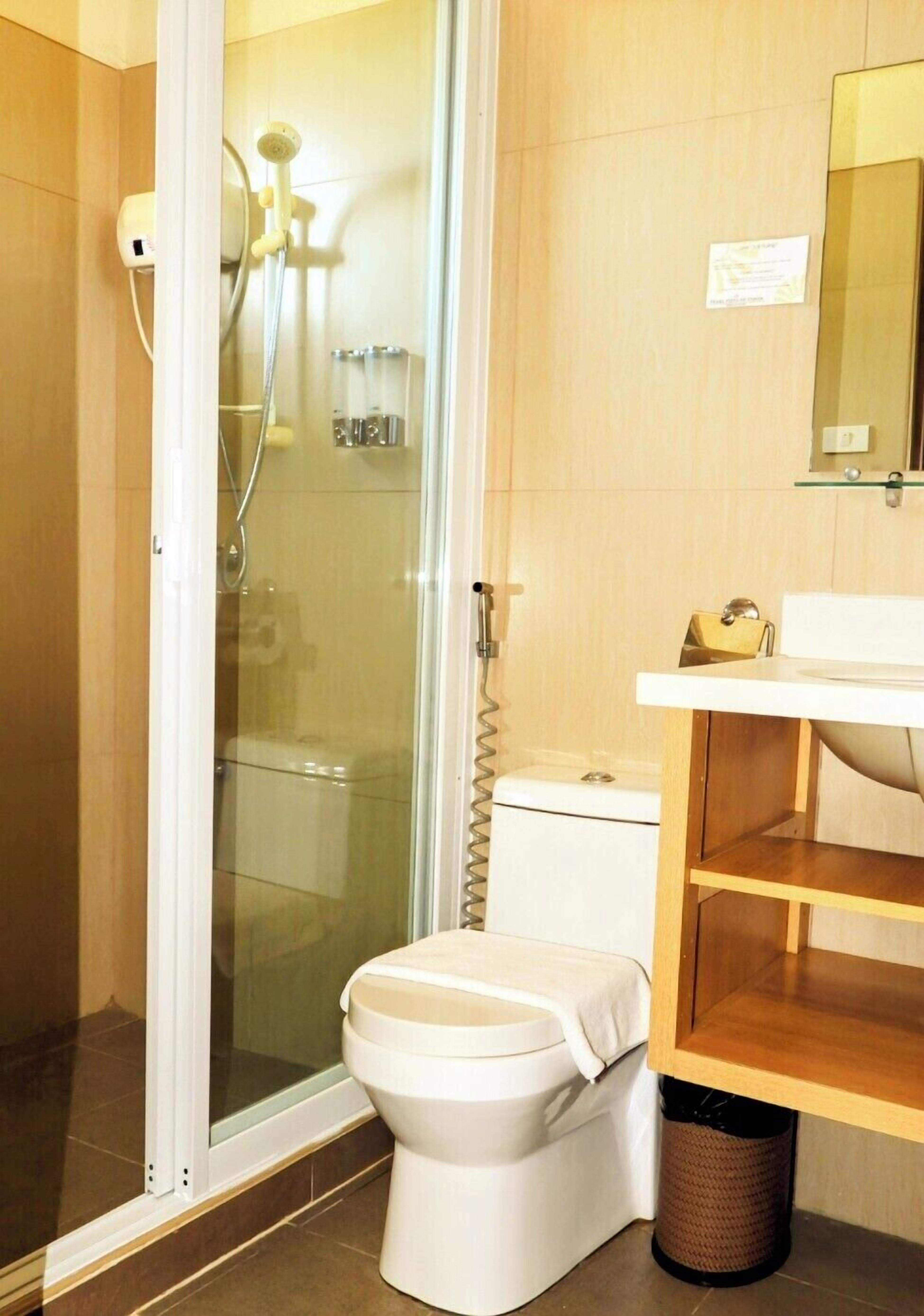 A bathroom with a glass-enclosed shower, a toilet, a sink with a mirror, and a trash can.