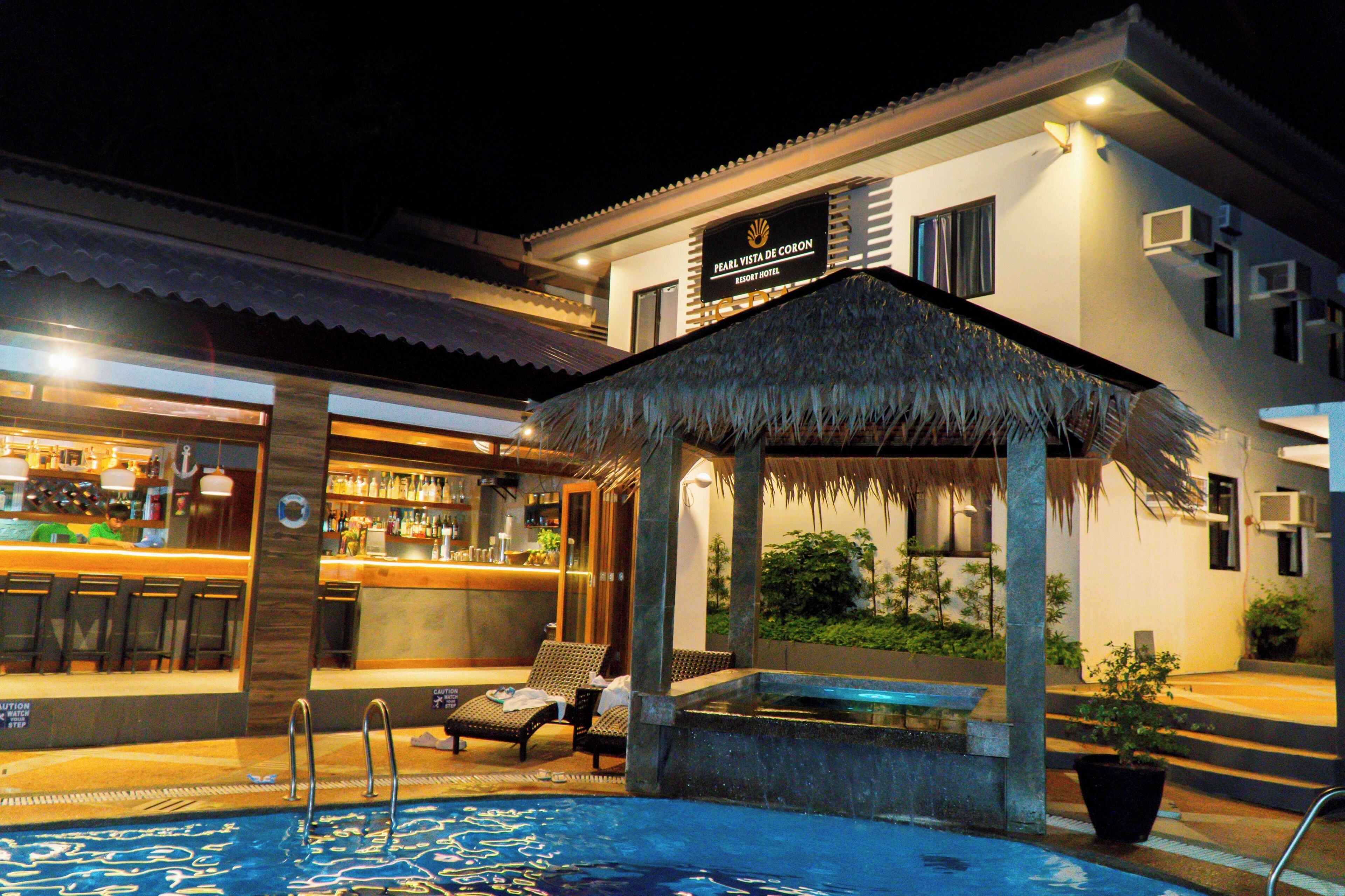 A resort hotel with a bar, lounge chairs, a pool, and a thatched-roof structure.