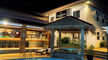 A resort hotel with a bar, lounge chairs, a pool, and a thatched-roof structure.