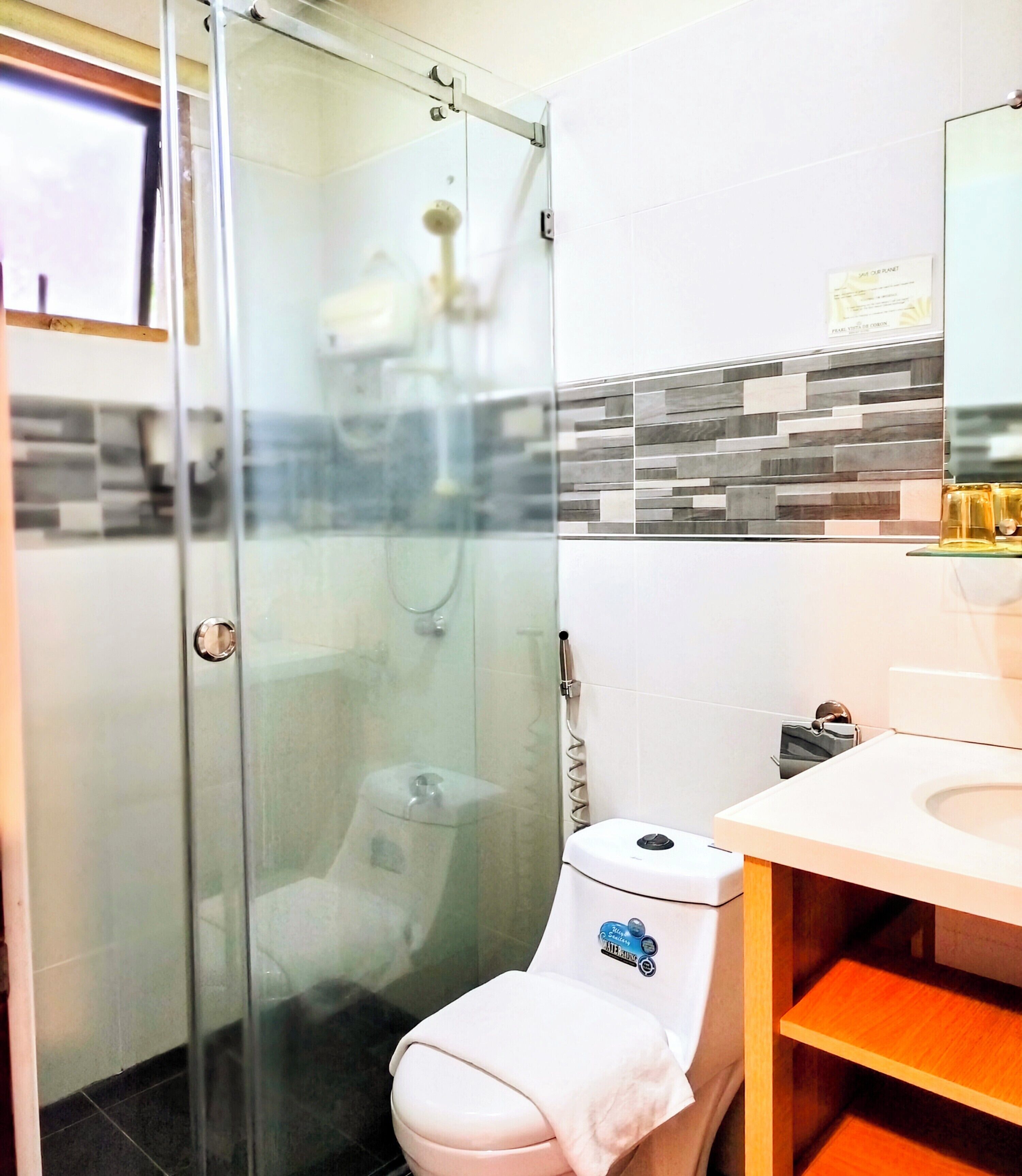 A modern bathroom with a glass-enclosed shower, a white toilet, and a sink with a mirror above it.