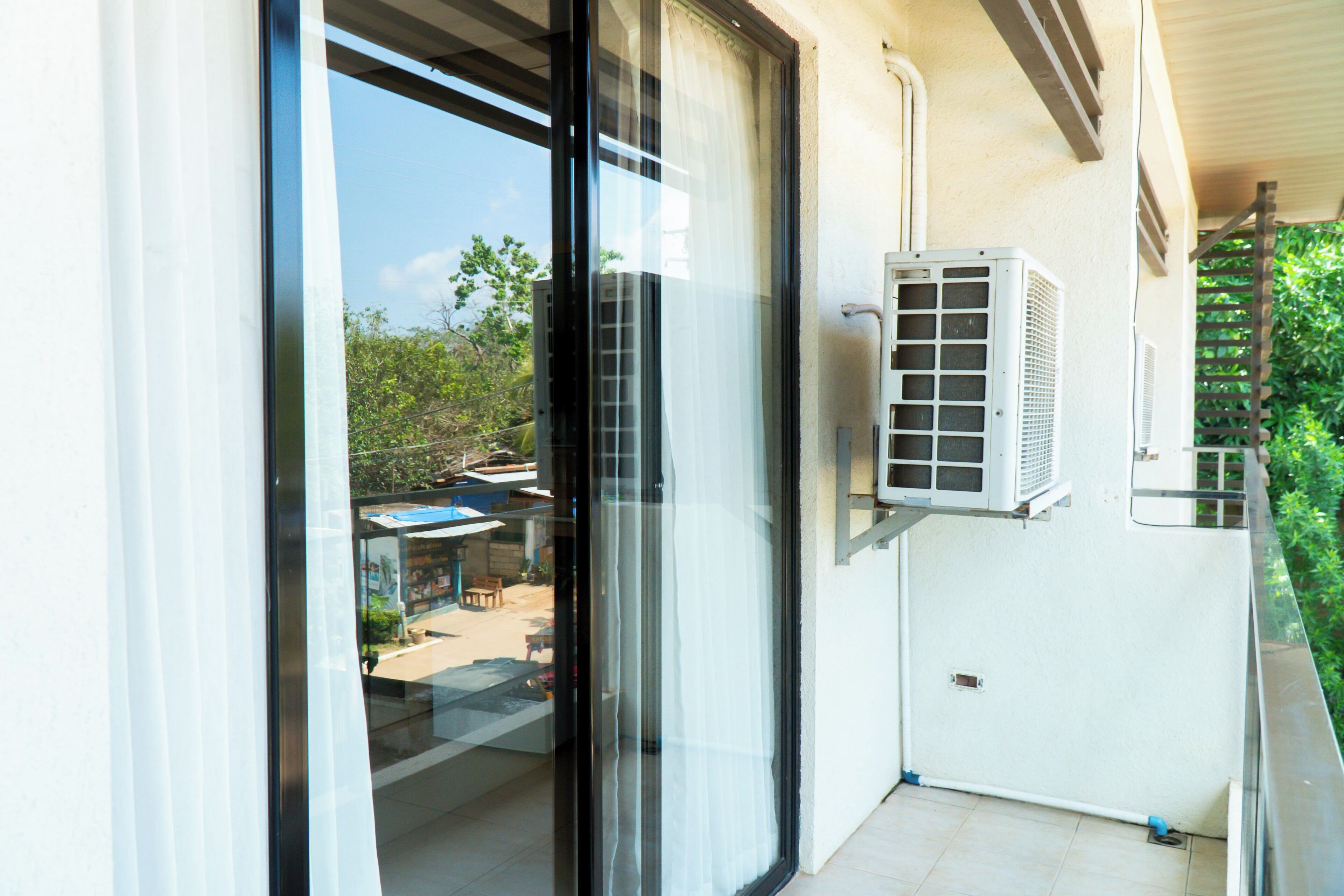 A balcony with a glass door, an air conditioning unit, and a view of a residential area.