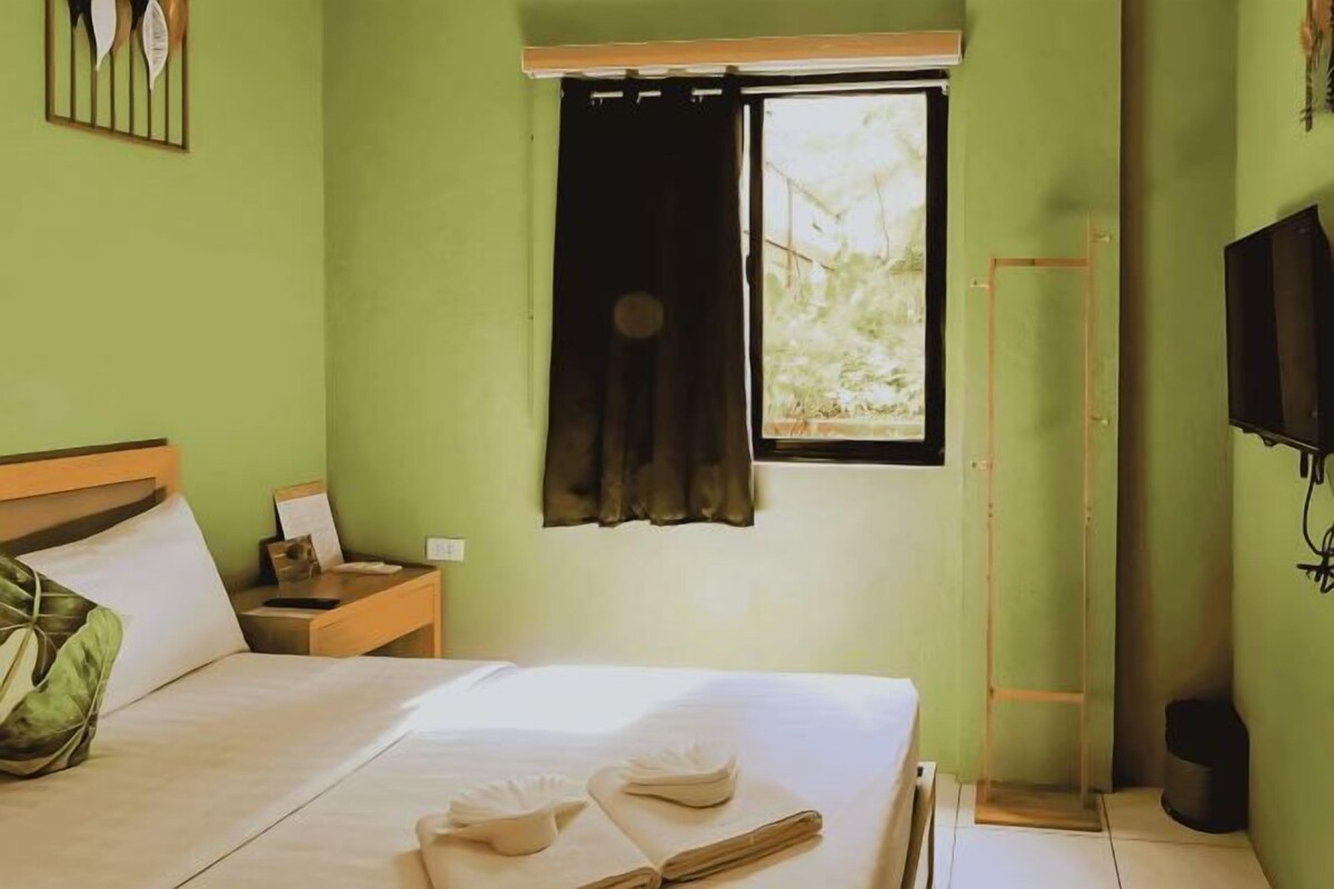 A hotel room with a bed, a nightstand, a window with curtains, a television, and a wooden ladder.