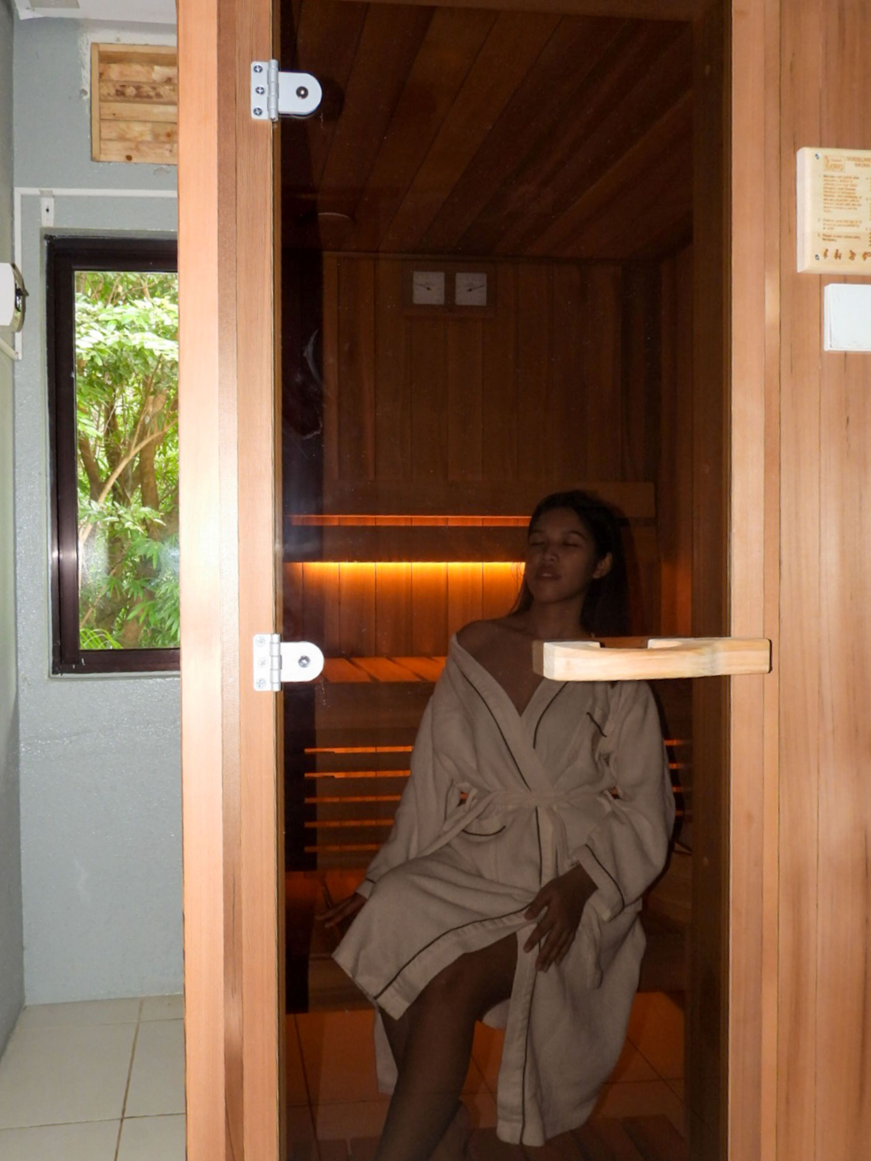 A person sitting in a wooden sauna with a bench and a shelf.