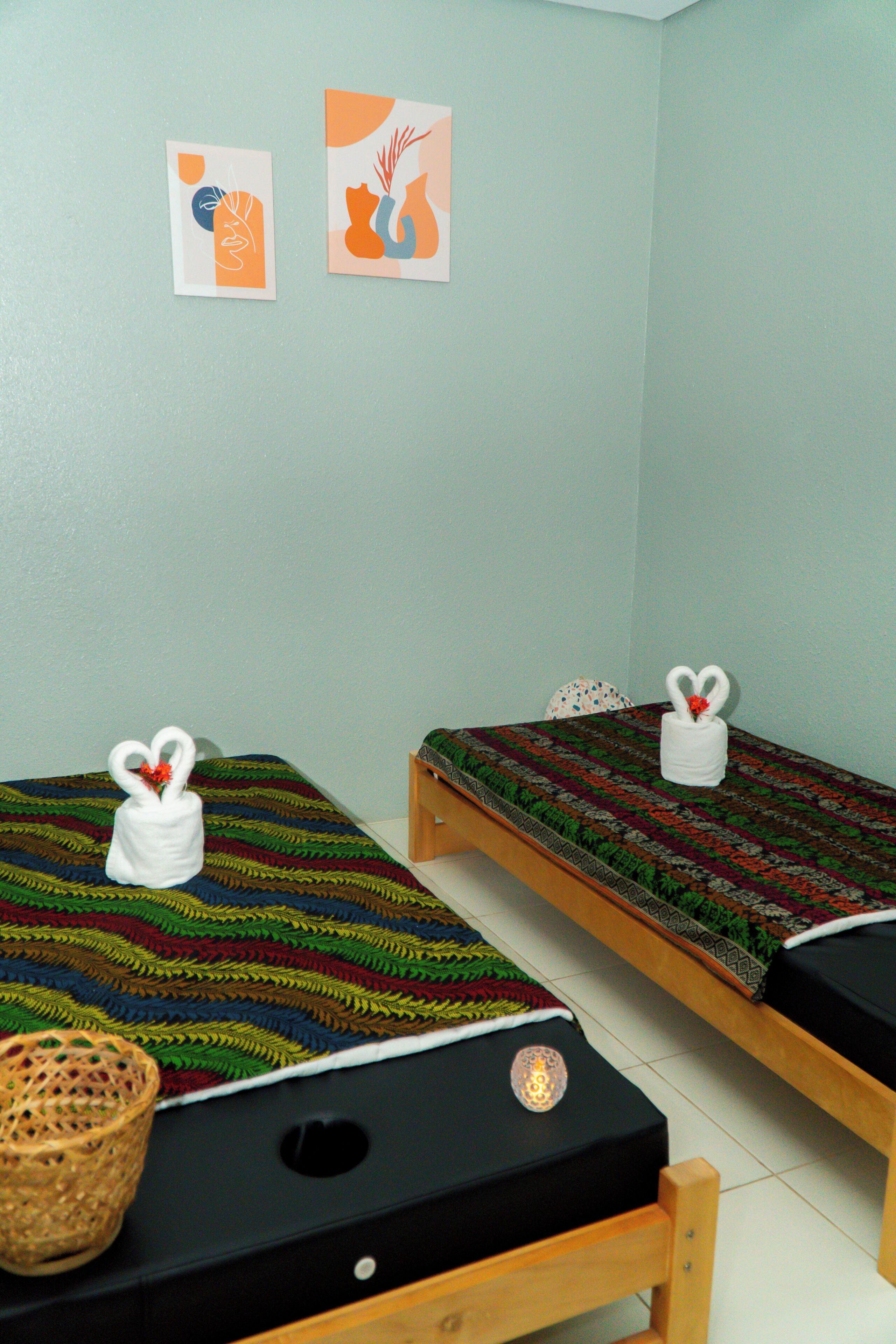 Two single beds with black mattresses and colorful blankets, a woven basket, and two wall art pieces.