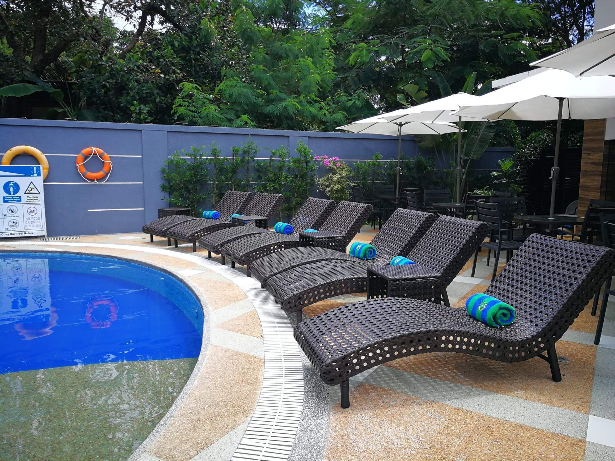 A poolside area with lounge chairs and umbrellas, a lifebuoy, and a sign with pool rules.