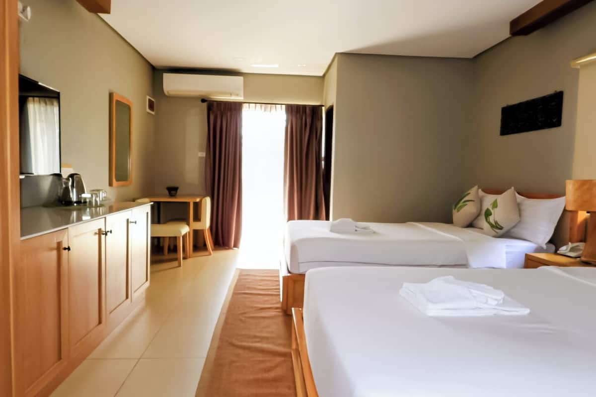 Quarto de hotel com duas camas, cozinha compacta, área de refeições e banheiro.