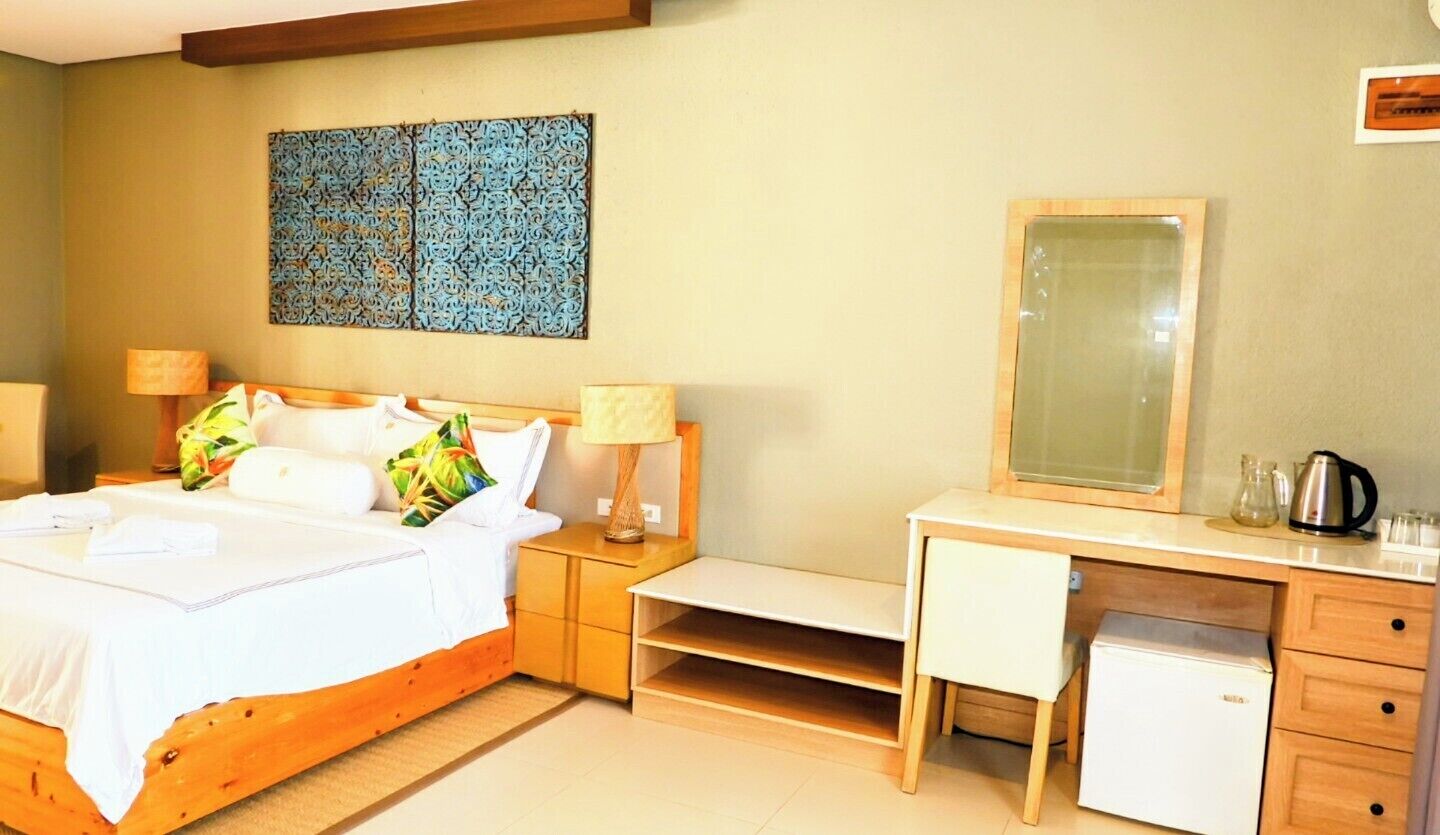 Ein Schlafzimmer mit Bett, Nachttischen, Schreibtisch, Stuhl, Spiegel und einem kleinen Kühlschrank.