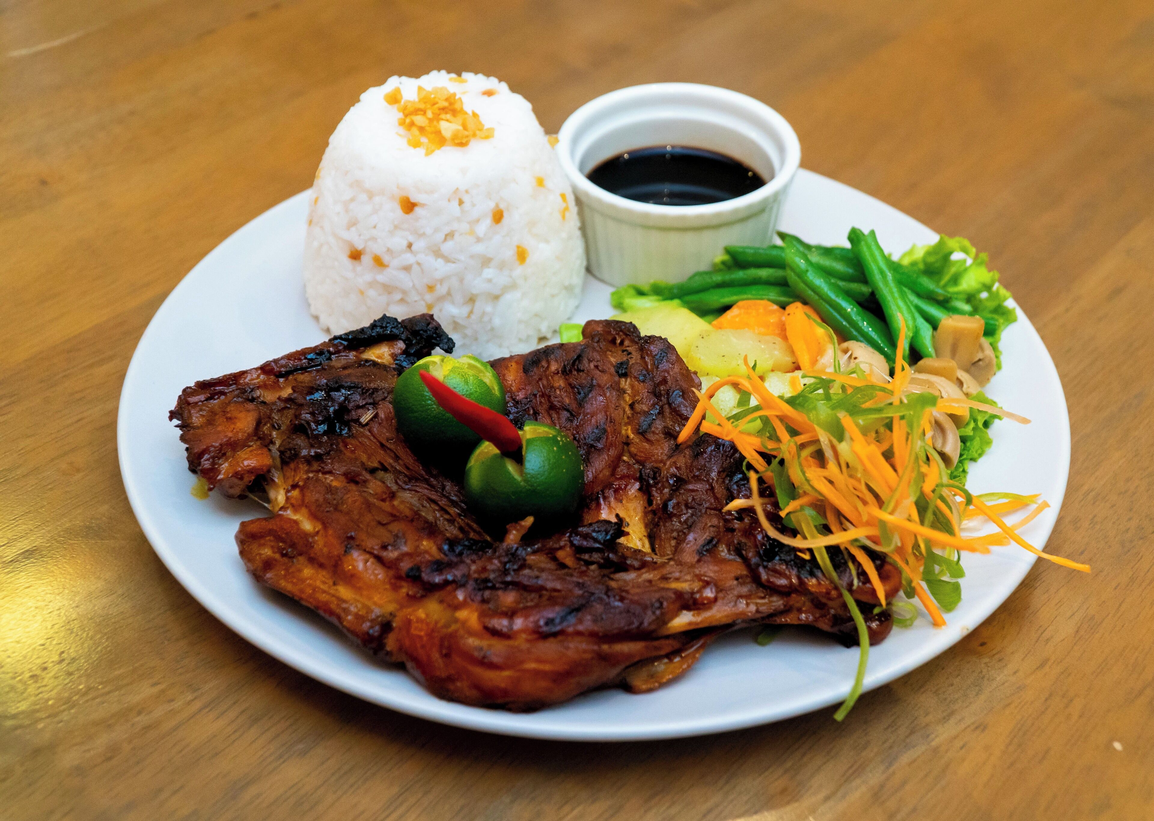 Une assiette de nourriture comprenant de la viande grillée, du riz, des légumes et un petit bol de sauce.