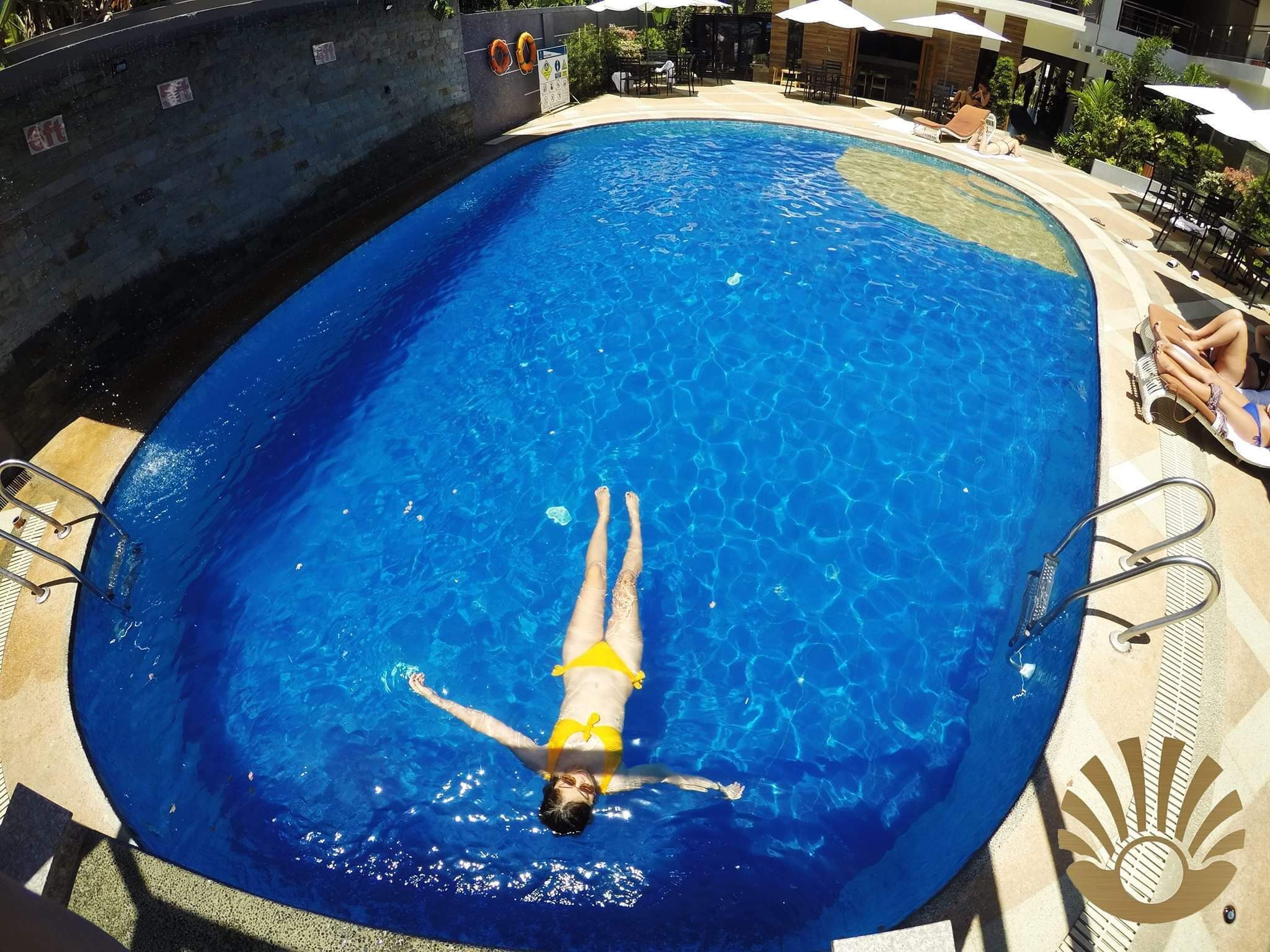 Une piscine où une personne nage, entourée de chaises longues et de parasols.