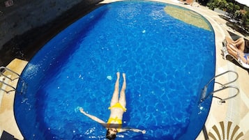 A swimming pool with a person swimming, surrounded by lounge chairs and umbrellas.
