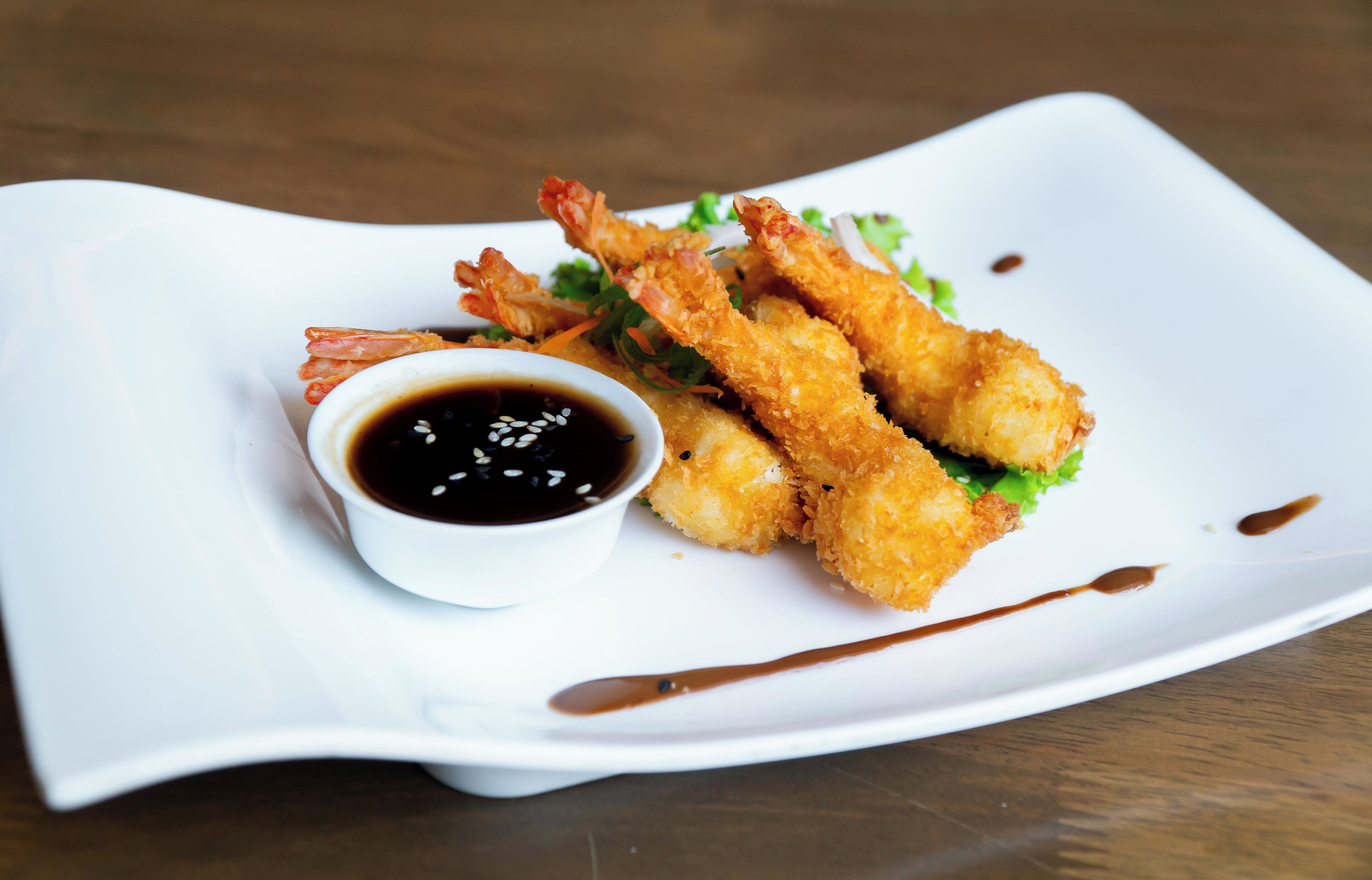 A white plate with fried shrimp and a small bowl of dipping sauce.