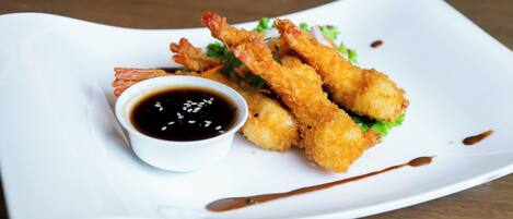 A white plate with fried shrimp and a small bowl of dipping sauce.