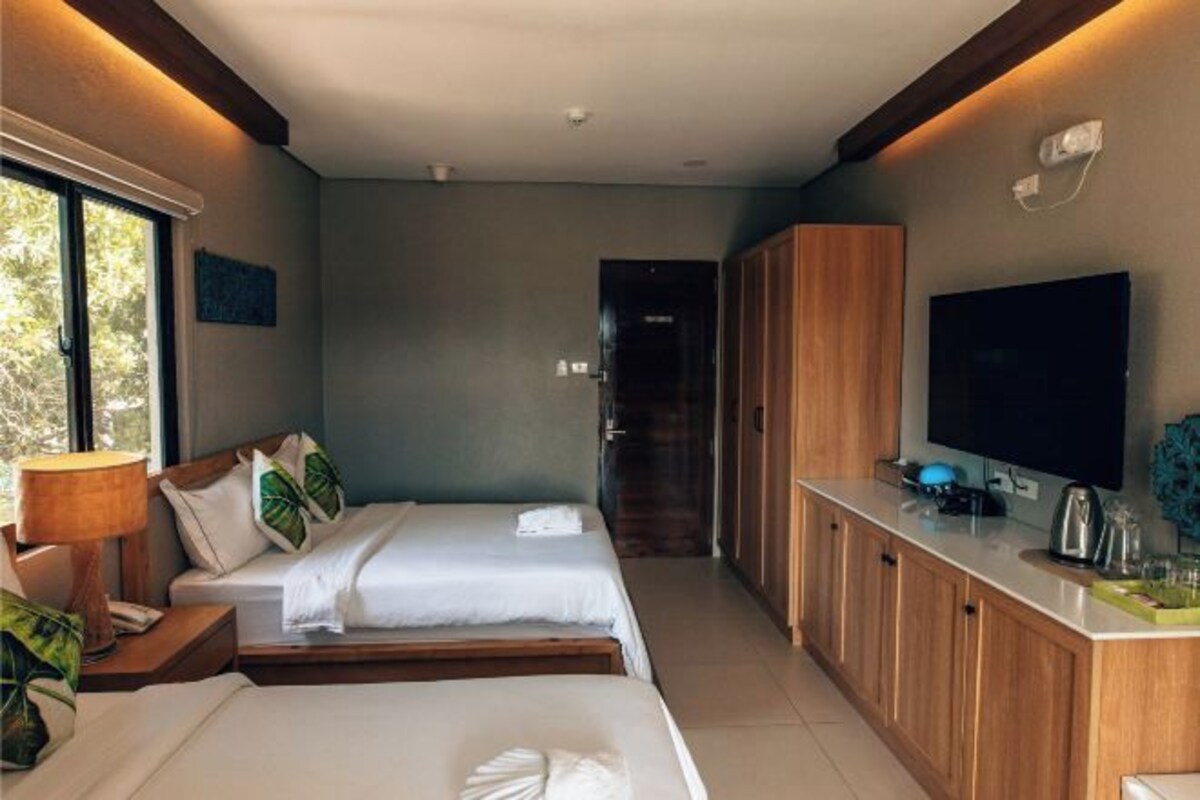 A hotel room with two beds, a TV, a wooden cabinet, and a window.