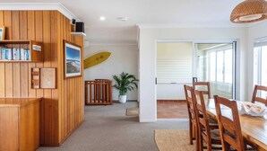 Um balcão de recepção de madeira, um prancha de surf, uma área de refeições com cadeiras de madeira e um vaso de planta.