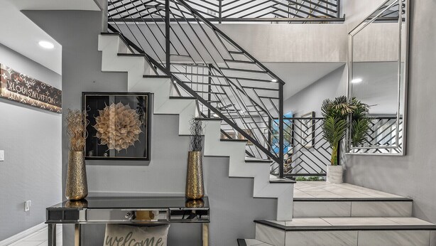 A modern staircase with a glass railing, a console table with a 'welcome' pillow, and a potted plant. - Spacious 4-bedroom house in charming Avondale with AC, WiFi (Avondale)
