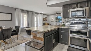 A modern kitchen with a central island, dark cabinets, stainless steel appliances, and a dining area with a table and chairs. - Spacious 4-bedroom house in charming Avondale with AC, WiFi (Avondale)