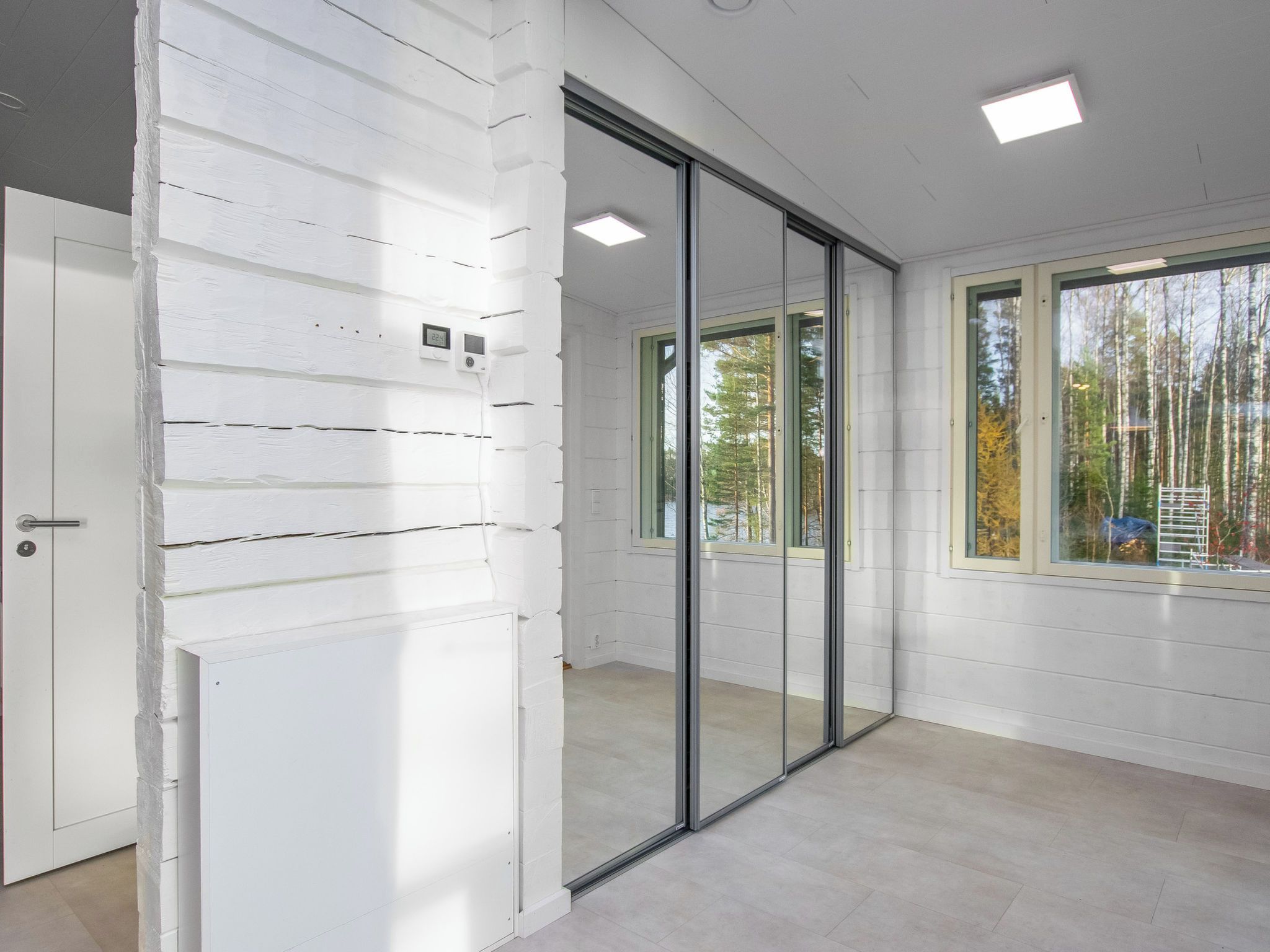 A room with white paneled walls, a sliding glass door, and a view of trees outside.