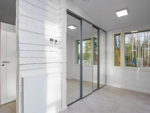 A room with white paneled walls, a sliding glass door, and a view of trees outside. - Villa milla by Interhome (Mäntyharju)