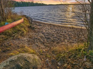 Une plage de sable avec un canoë rouge et un grand rocher.