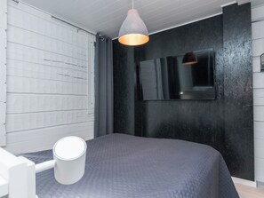 Ett modernt sovrum med en säng, ett vitt sängbord, en grå vägg med struktur, en svart accentvägg och en hängande taklampa.