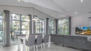 Ein modernes Interieur mit Essbereich, einer Couch und großen Fenstern mit Blick auf Bäume.