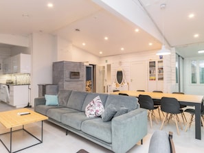 Un salon moderne avec un canapé gris, une table basse en bois et un coin repas comprenant une longue table et des chaises.
