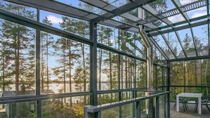 Eine moderne, gläserne Struktur mit Holzterrasse, großen Fenstern und einem Tisch mit Stühlen.