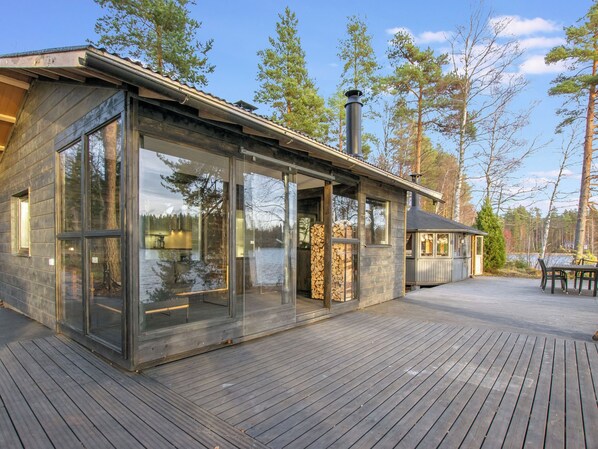 A modern cabin with large glass windows, a deck, and a chimney.