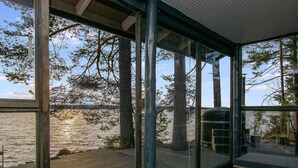 Eine Holzterrasse mit Glasumrandung, die auf einen See mit umliegenden Bäumen blickt.