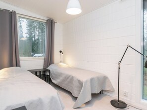 Une chambre avec deux lits, un bureau, une lampe et une fenêtre avec des rideaux.