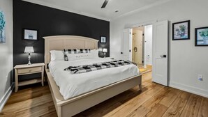 Et soveværelse med seng, natbord, lampe, loftventilator og en dør til et andet rum.