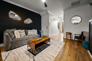 Una sala de estar moderna con un sofá gris, una mesa de centro de madera y una pared de acento negra.