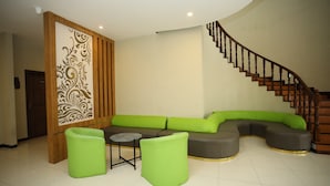 A modern living room with a curved staircase, a sectional sofa, and two green poufs. - Parkside Meuligoe Hotel (Meulaboh)