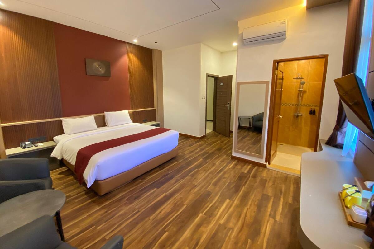 A hotel room with a large bed, wooden flooring, a shower area, and a seating area with a table and chairs.