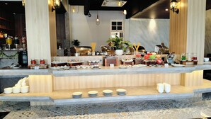 A buffet setup with various food items and drinks, a coffee machine, and a potted plant. - Parkside Meuligoe Hotel (Meulaboh)