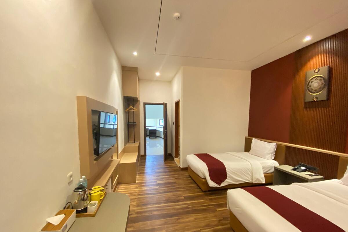 A hotel room with two beds, a TV, a desk with a tray, and a wooden floor.