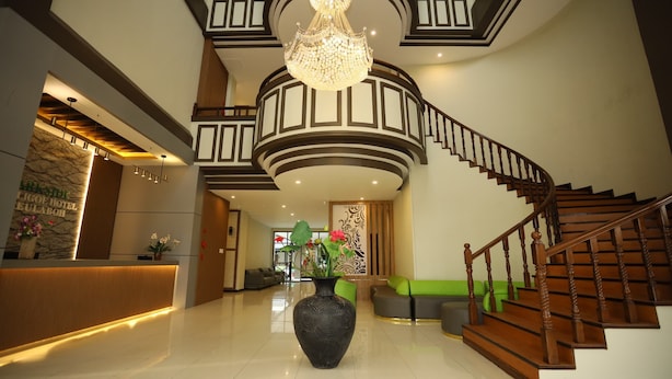 A spacious lobby with a reception desk, a large vase with flowers, a grand staircase, and a chandelier. - Parkside Meuligoe Hotel (Meulaboh)