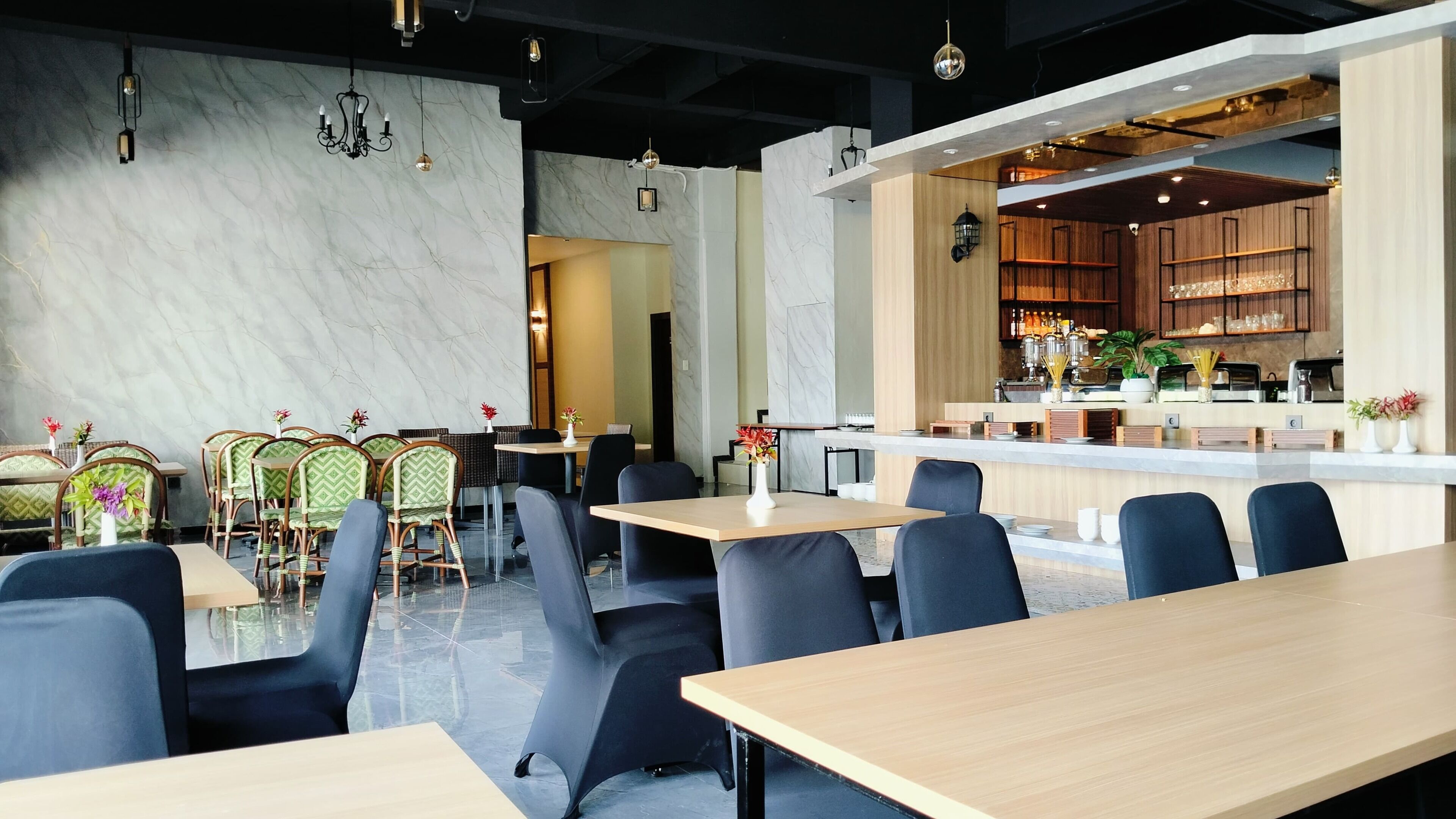 A modern restaurant with marble walls, a bar area, and a mix of seating styles including tables and chairs.