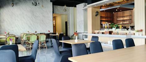 A modern restaurant with marble walls, a bar area, and a mix of seating styles including tables and chairs.